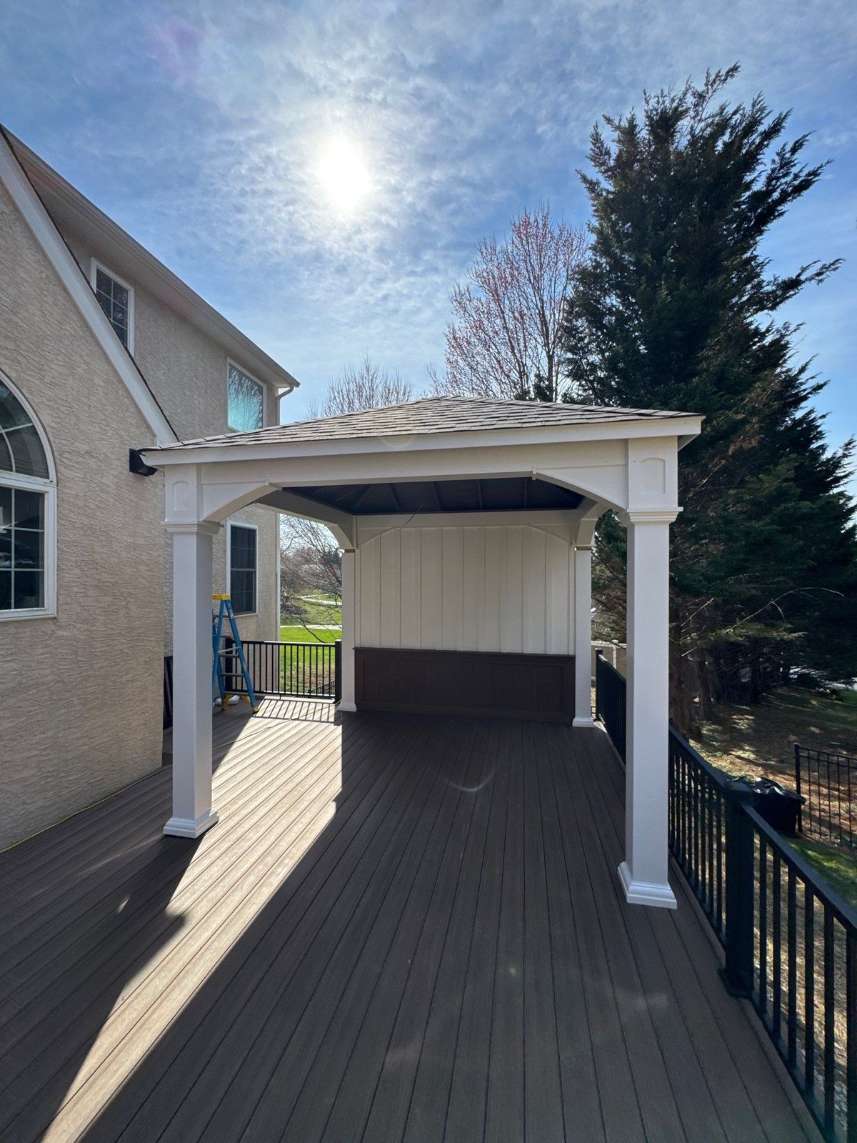 Brown composite covered deck with a white-columned pavilion at a stucco home in Chester County, PA