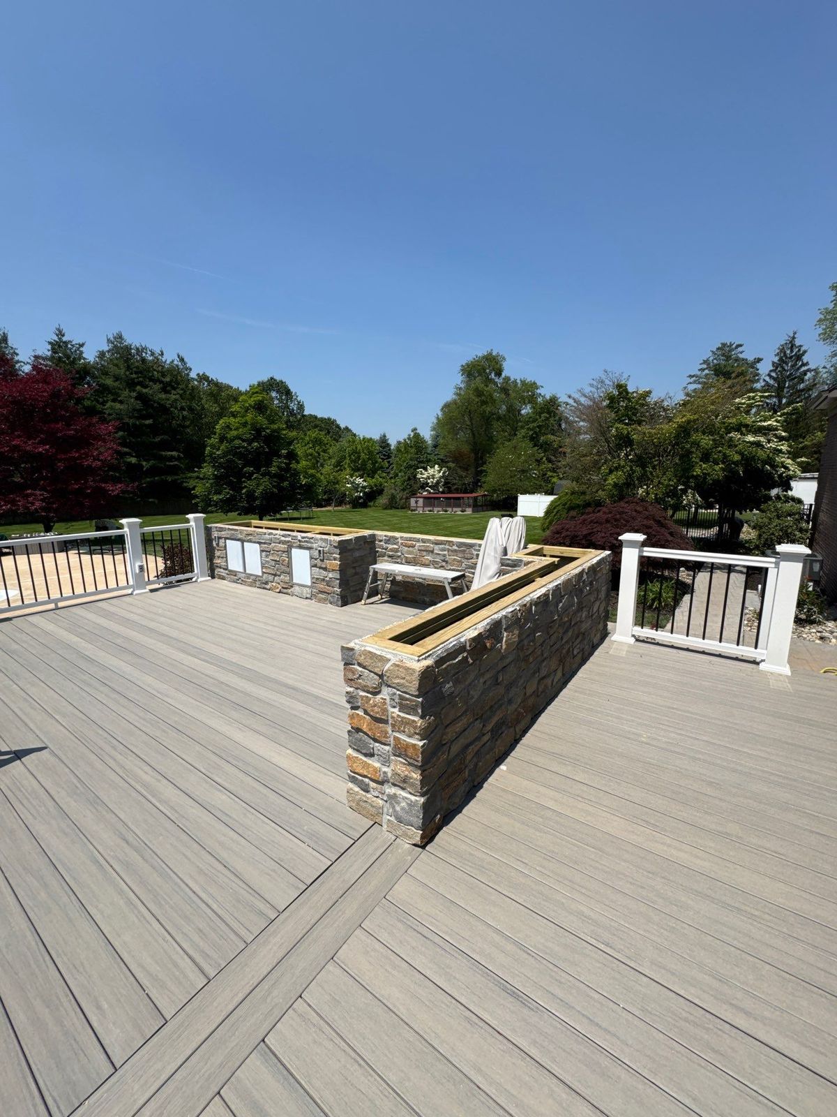 Gray composite deck with natural stone seat walls and black aluminum railing in a Main Line PA backyard