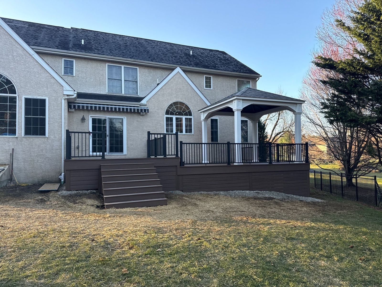 Brown composite deck with a covered porch section and black aluminum railing on a stucco home in Newtown Square, PA