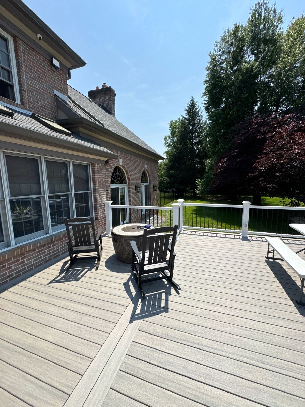 Light gray composite deck with fire pit and rocking chairs behind a brick home in Delaware County, PA