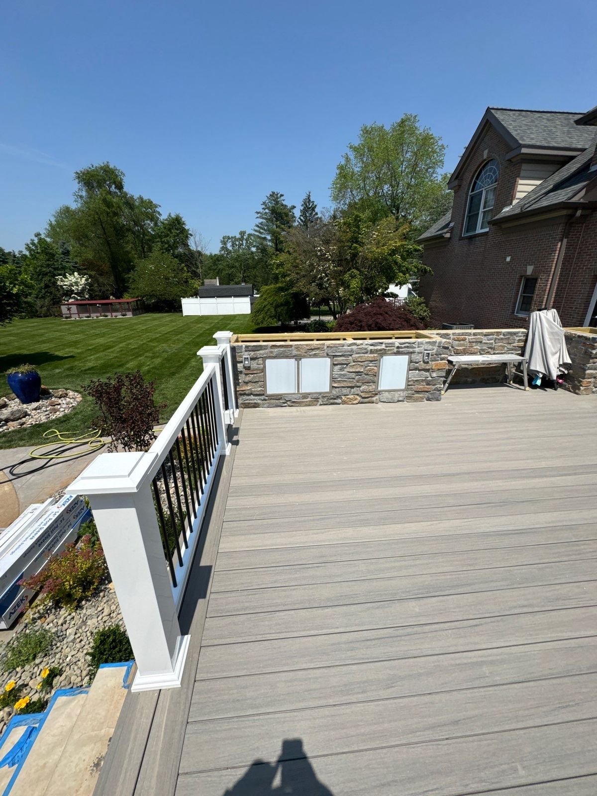 Gray composite deck with white railing and stone veneer accent wall at a brick home in Newtown Square, PA