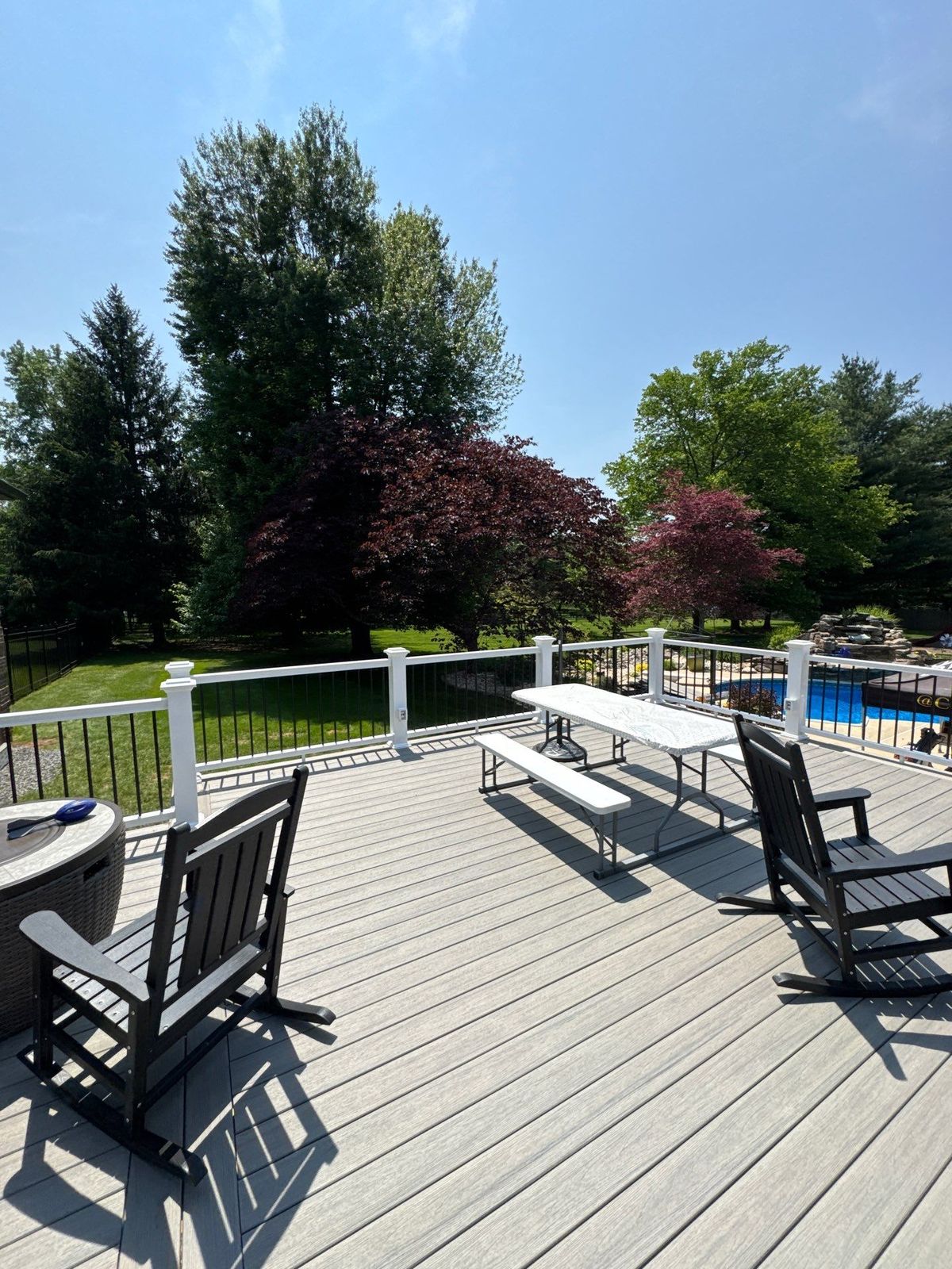 Light gray composite deck overlooking a backyard pool with white railing in Delaware County, PA