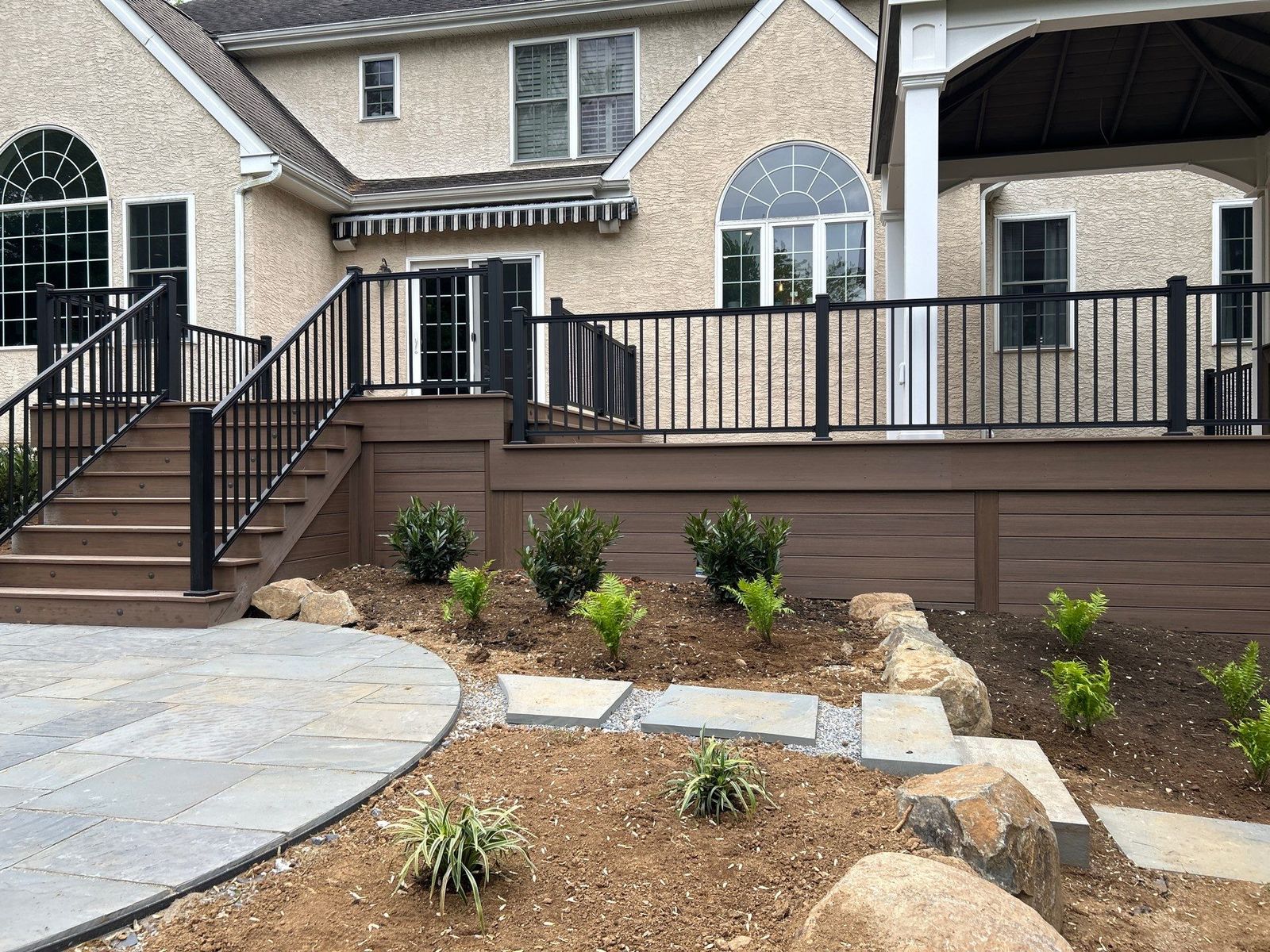 Raised brown composite deck with stairs, black railing and flagstone walkway at a stucco home in Newtown Square, PA